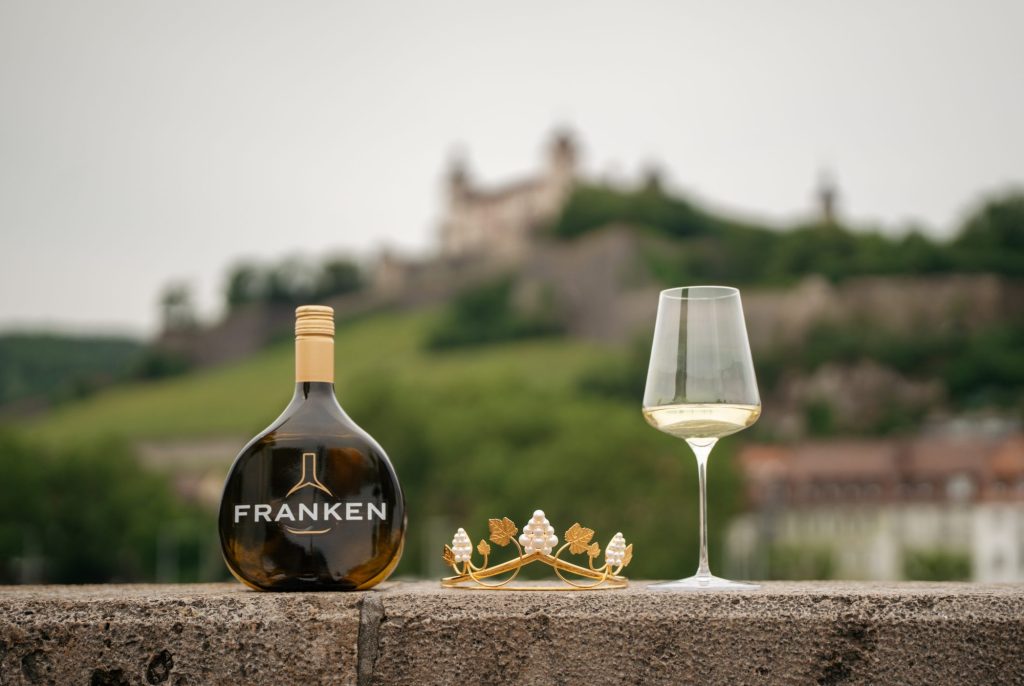 Krone der Fränkischen Weinkönigin inmitten eines Glas Silvaner und einem Bocksbeutel. Foto: Daniel Oppelt / Gebietsweinwerbung Frankenwein-Frankenland GmbH
